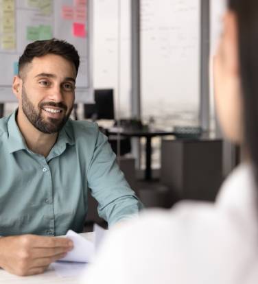 Recruiter holding resume and listening female, vacancy candidature seated at table in modern office, feel satisfied with answers about education, professional knowledge and experience